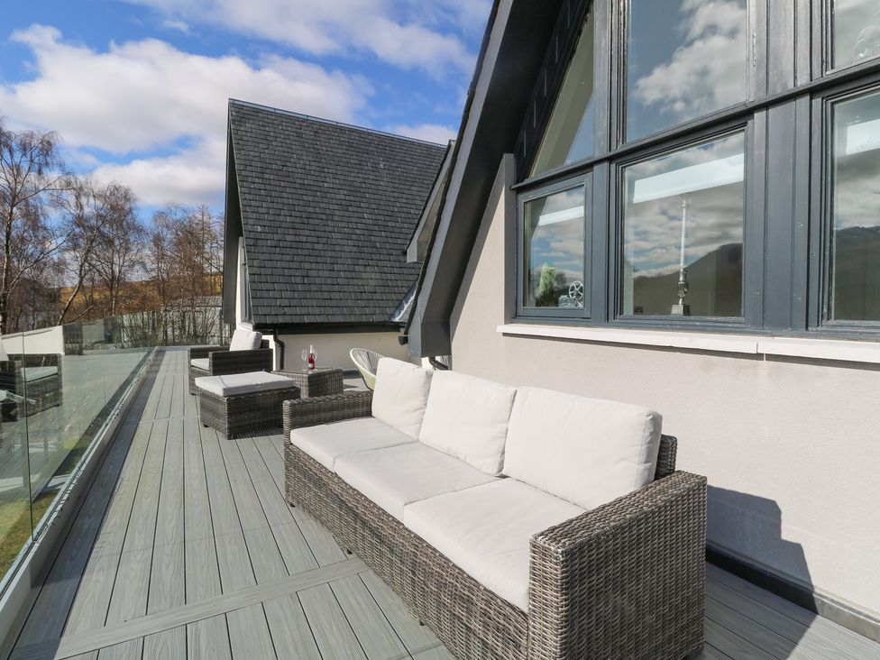 An outdoor balcony with woven sofas and armchairs a glass railing and a sloped roof at Macgregor Ranch in Achnabobane near Spean Bridge