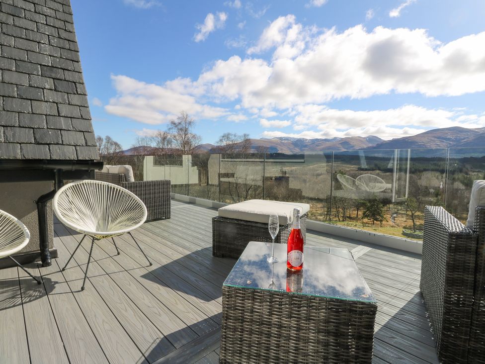 A patio with chairs a glass table with a bottle and glass and a view of mountains at Macgregor Ranch in Achnabobane near Spean Bridge