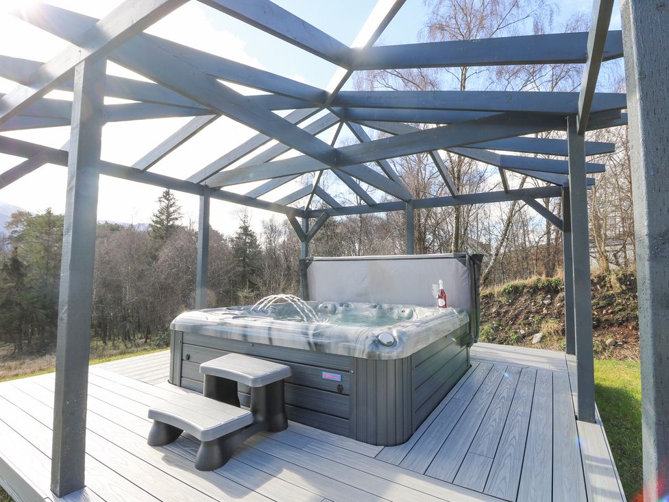 An outdoor hot tub with water jets on a wooden deck under a wooden pergola at Macgregor Ranch in Achnabobane near Spean Bridge