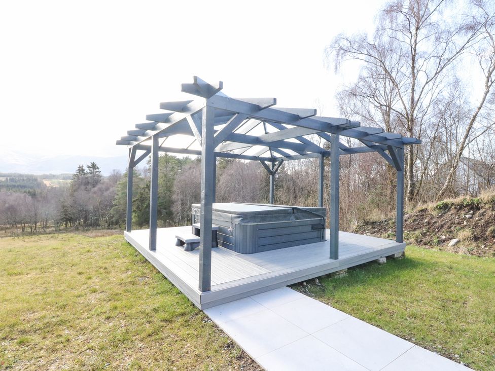 An outdoor wooden deck with a covered hot tub on a grassy area at Macgregor Ranch in Achnabobane near Spean Bridge