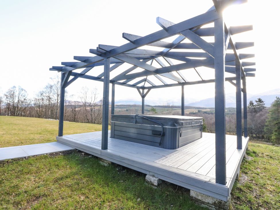 An outdoor hot tub on a wooden deck under a pergola in a grassy area at Macgregor Ranch in Achnabobane near Spean Bridge
