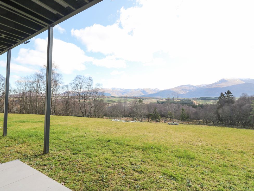 A grassy field with trees and distant mountains seen from under a covered patio at Macgregor Ranch in Achnabobane near Spean Bridge