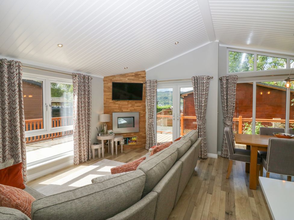 A living room with a grey sofa and wood floor next to a dining area with a wooden table and grey chairs at Waterside Lodge 55A Bowness White Cross Bay near Windermere