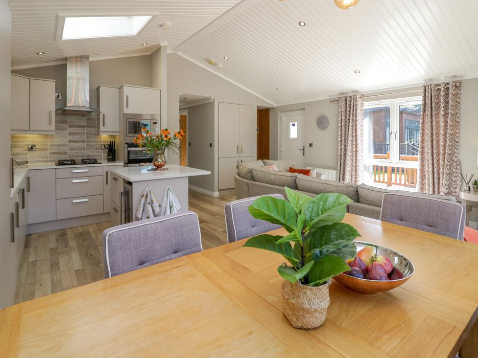 A kitchen with an island and a dining table with chairs and a plant and fruit bowl at Waterside Lodge 55A Bowness White Cross Bay near Windermere