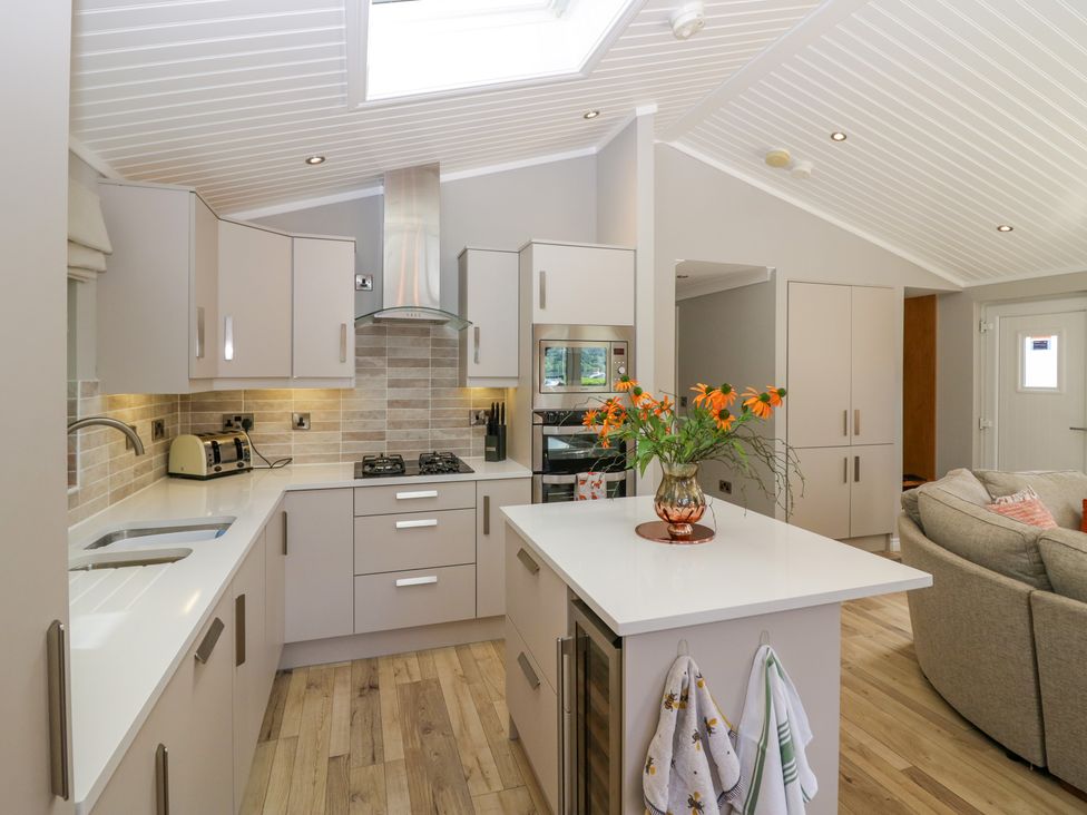 A kitchen with white countertops a vase with flowers a gas stove and a dining area at Waterside Lodge 55A Bowness White Cross Bay near Windermere