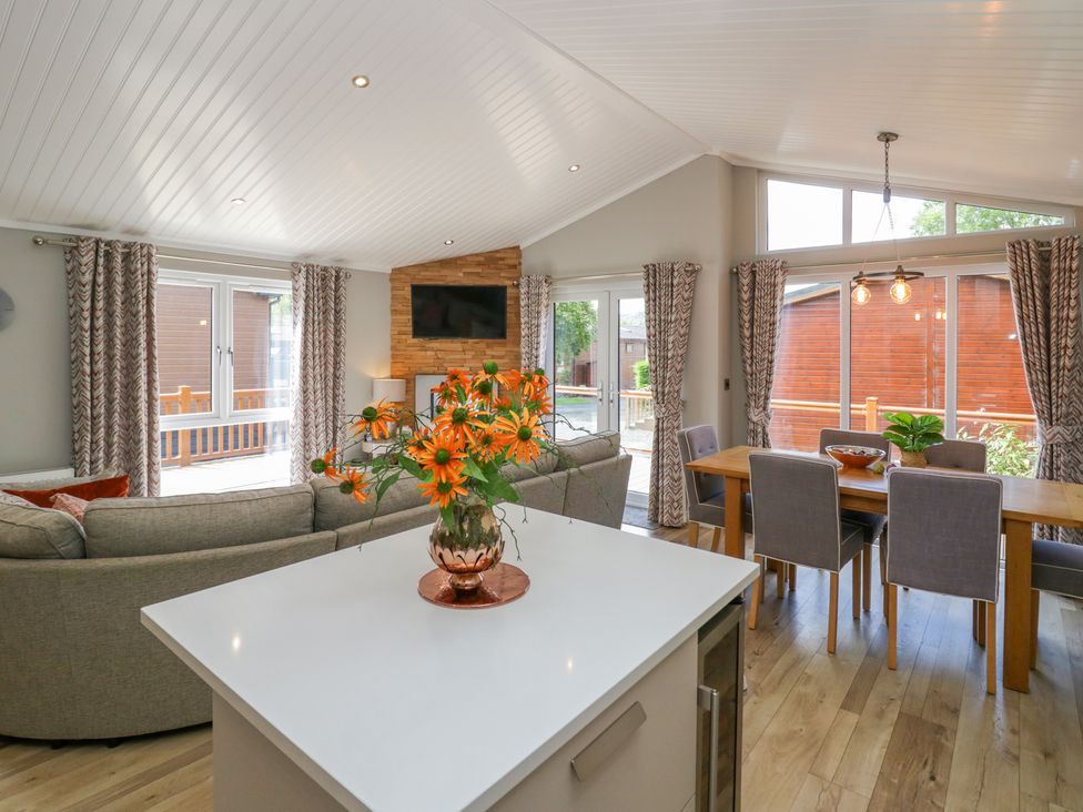 A living area with a sofa and a television mounted on a wooden accent wall and a dining table with chairs at Waterside Lodge 55A Bowness White Cross Bay near Windermere