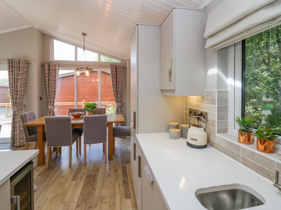 A kitchen with a white countertop and sink next to a dining table with six chairs at Waterside Lodge 55A Bowness White Cross Bay near Windermere