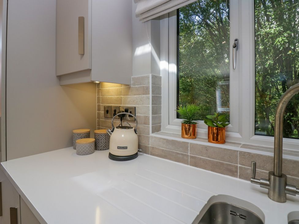 A kitchen countertop with a white kettle three canisters two small plants on the windowsill and a faucet at Waterside Lodge 55A Bowness White Cross Bay near Windermere