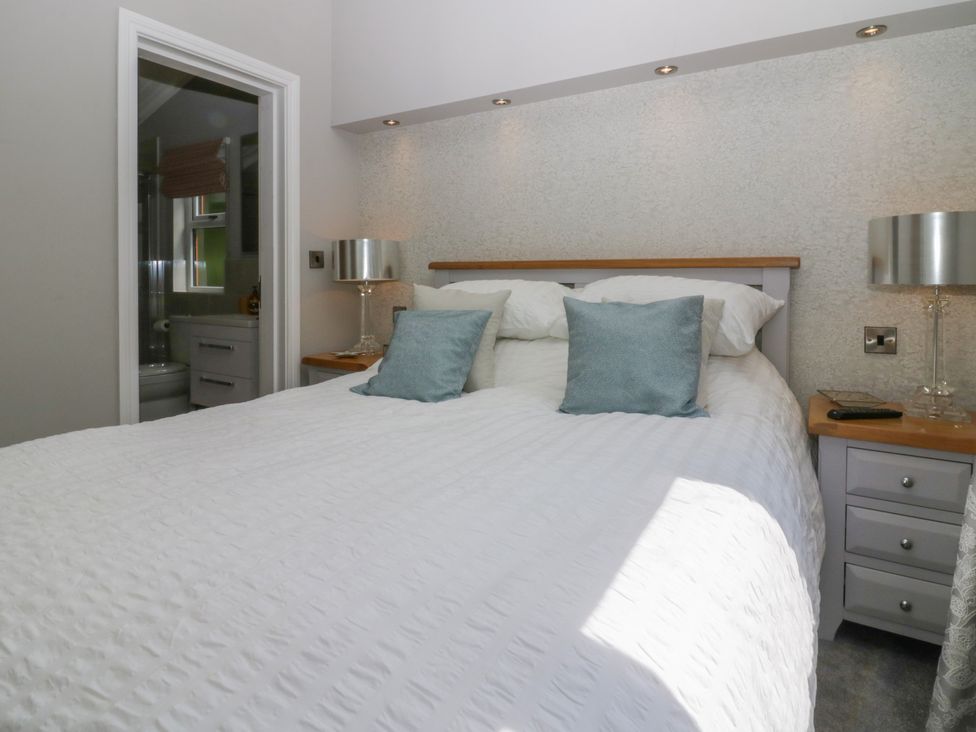 A bedroom with a white bedspread blue pillows two bedside tables with silver lamps and an ensuite bathroom at Waterside Lodge 55A Bowness White Cross Bay near Windermere
