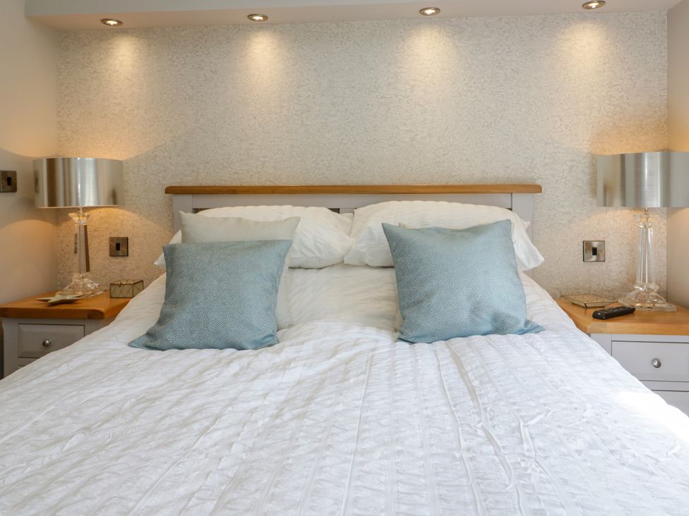 A bed with white bedding and blue pillows with bedside tables and lamps at Waterside Lodge 55A Bowness White Cross Bay near Windermere