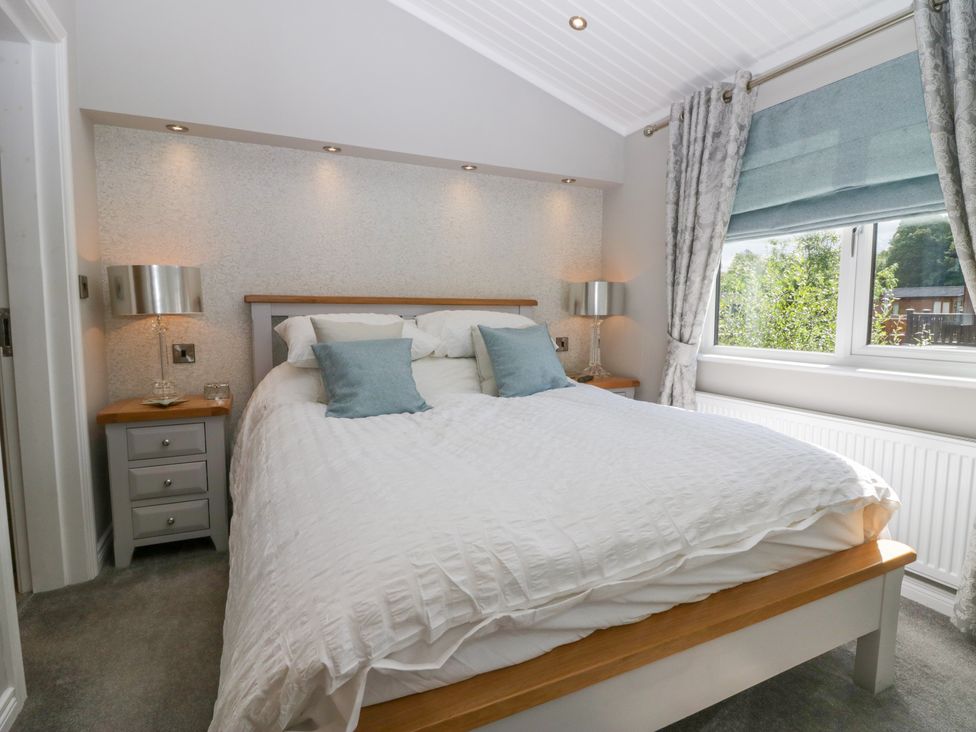 A bedroom with a double bed two bedside tables with lamps a window with curtains and a roman blind at Waterside Lodge 55A Bowness White Cross Bay near Windermere