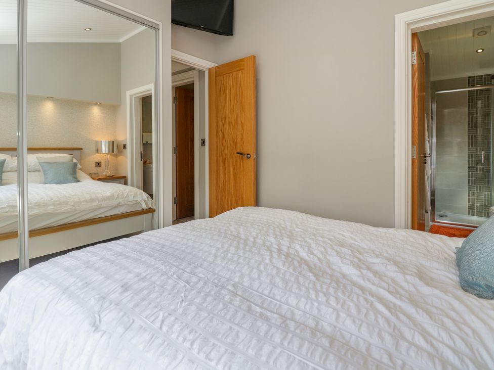 A bedroom with a bed a wooden door and a mirrored wardrobe at Waterside Lodge 55A Bowness White Cross Bay near Windermere