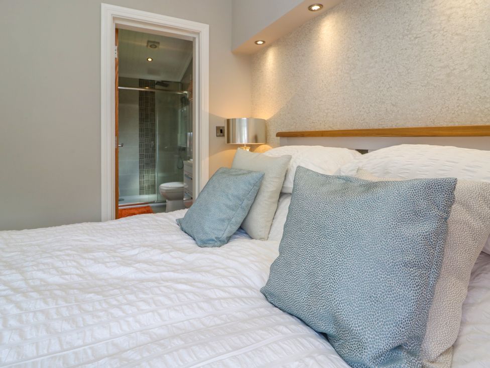 A bedroom with a bed and cushions and a view of an en suite bathroom at Waterside Lodge 55A Bowness White Cross Bay near Windermere
