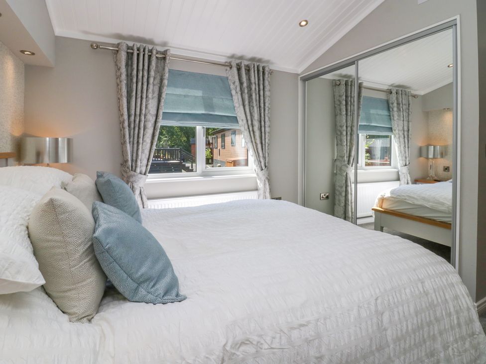 A bedroom with a bed with pillows a window with curtains and a mirrored wardrobe at Waterside Lodge 55A Bowness White Cross Bay near Windermere