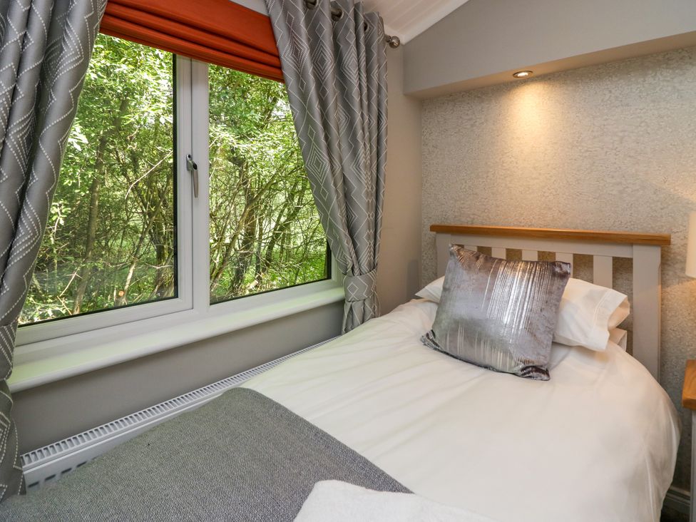 A single bed with a pillow and bedding next to a window with curtains at Waterside Lodge 55A Bowness White Cross Bay near Windermere