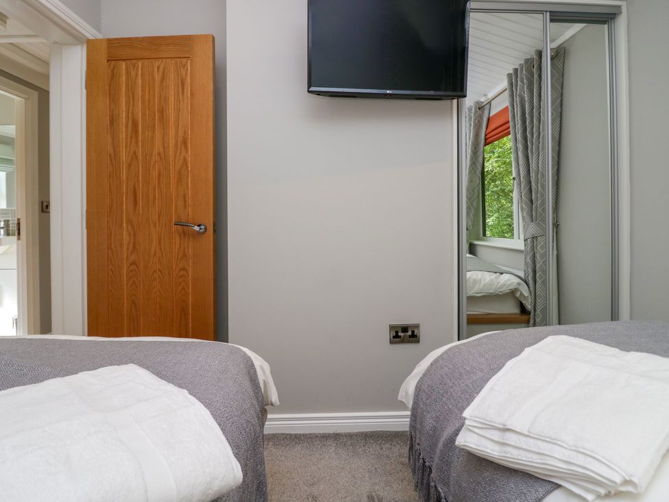 A bedroom with two single beds a wooden door a wall-mounted television and a mirrored wardrobe at Waterside Lodge 55A Bowness White Cross Bay near Windermere