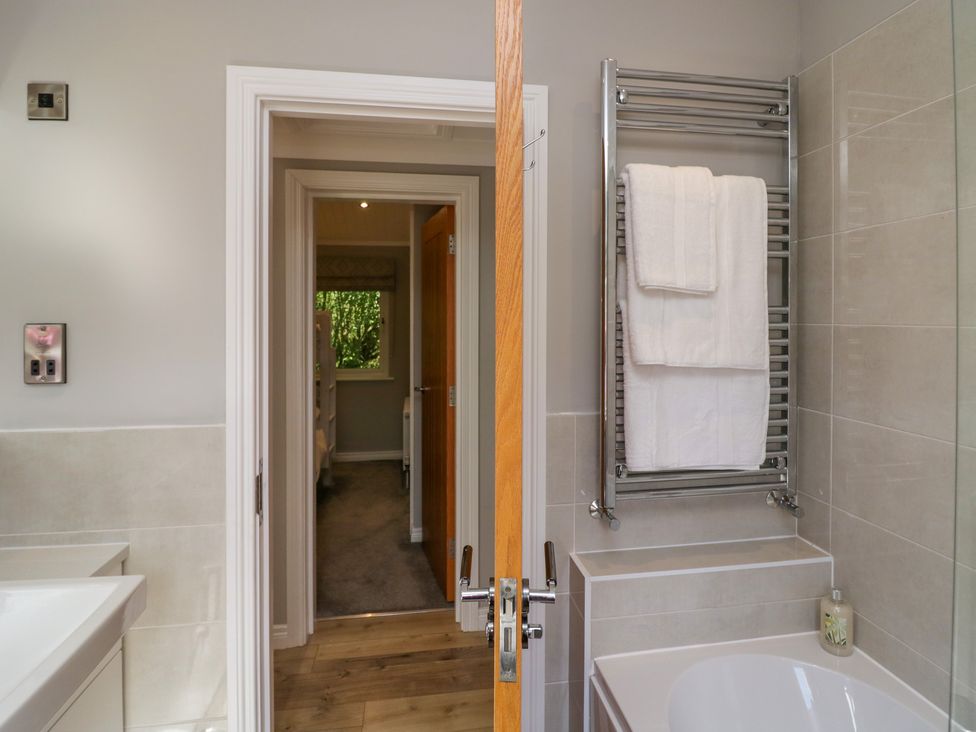 A bathroom with a towel rack holding white towels and a bathtub next to a doorway showing a hallway at Waterside Lodge 55A Bowness White Cross Bay near Windermere