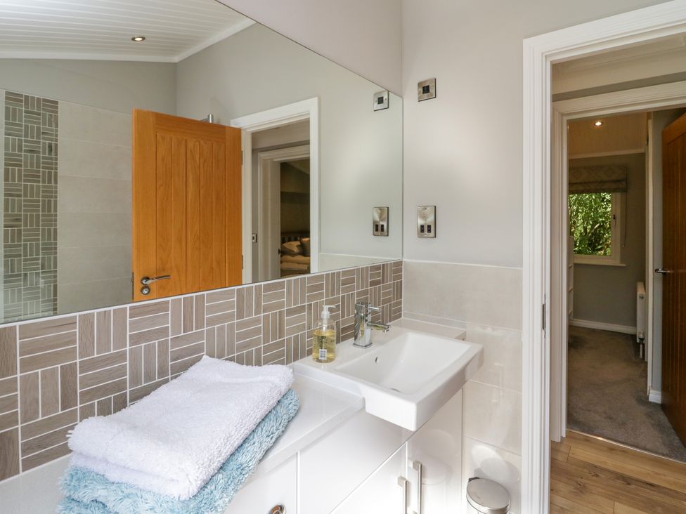 A bathroom with a sink a mirror folded towels and a door open to a hallway at Waterside Lodge 55A Bowness White Cross Bay near Windermere