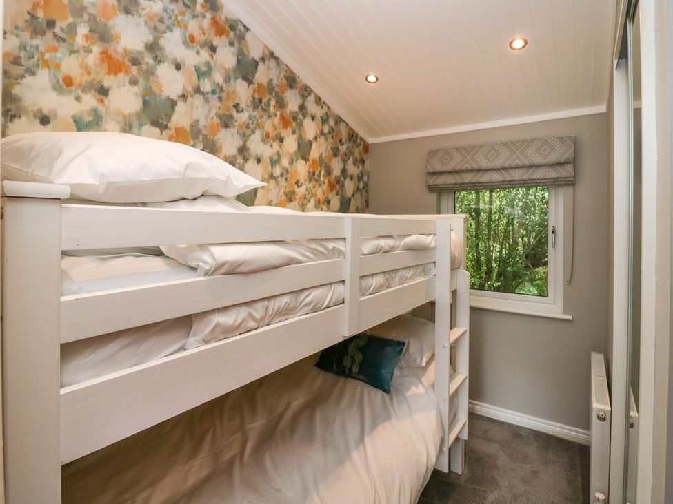 A bedroom with white bunk beds a window with a patterned blind and floral wallpaper at Waterside Lodge 55A Bowness White Cross Bay near Windermere