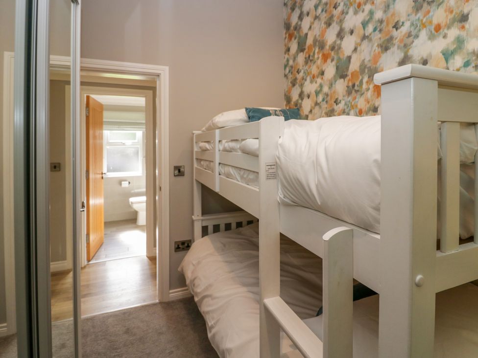 A bedroom with white bunk beds and floral wallpaper near a bathroom at Waterside Lodge 55A Bowness White Cross Bay near Windermere