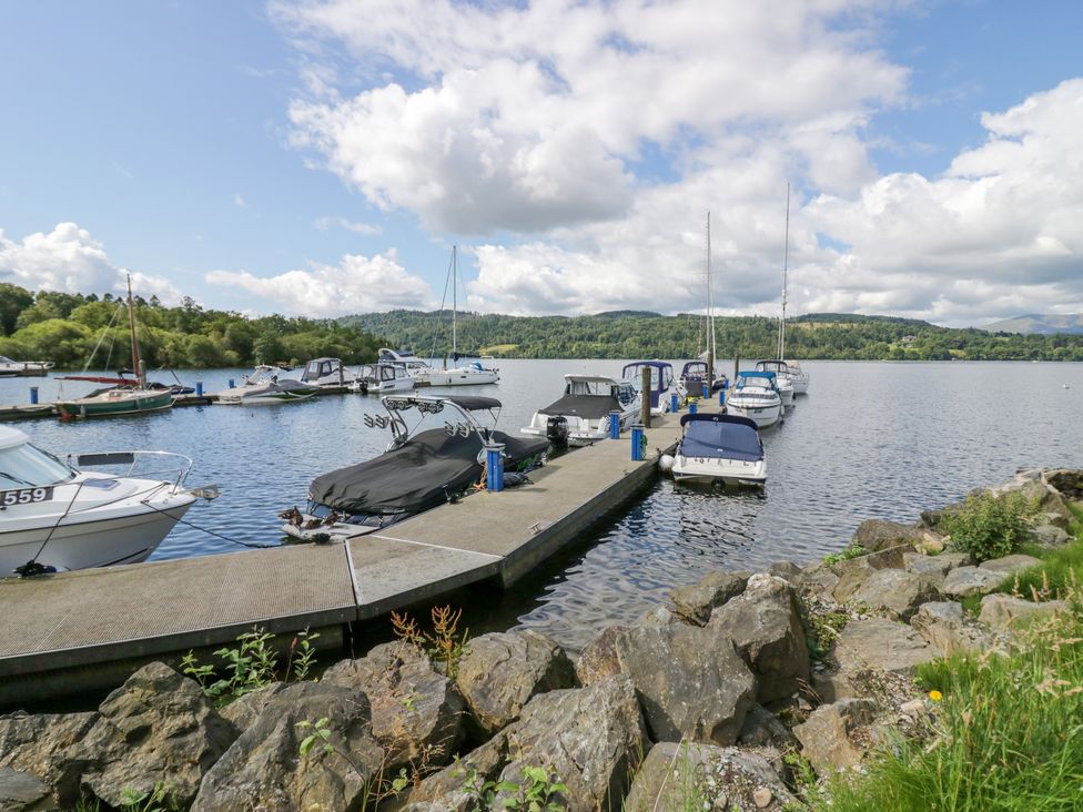 A dock with boats moored on a lake with hills and trees in the background at Waterside Lodge 55A Bowness White Cross Bay near Windermere