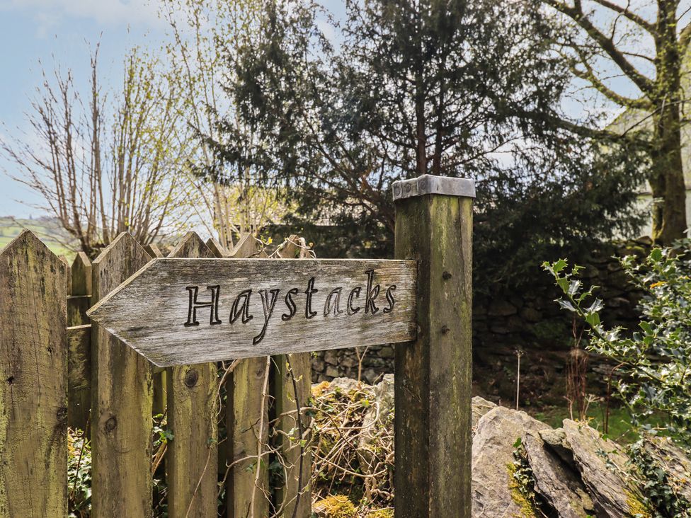 A sign labeled Haystacks with a wooden fence and trees in the background at Haystacks in Troutbeck