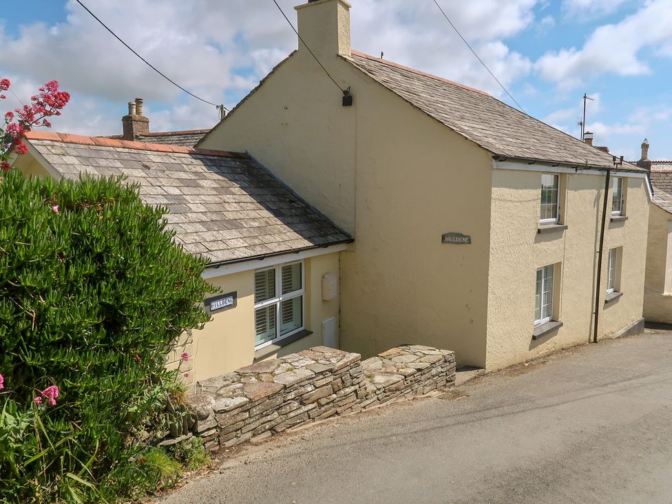 A yellow house with a stone wall and a sign at Hilldene in Treknow