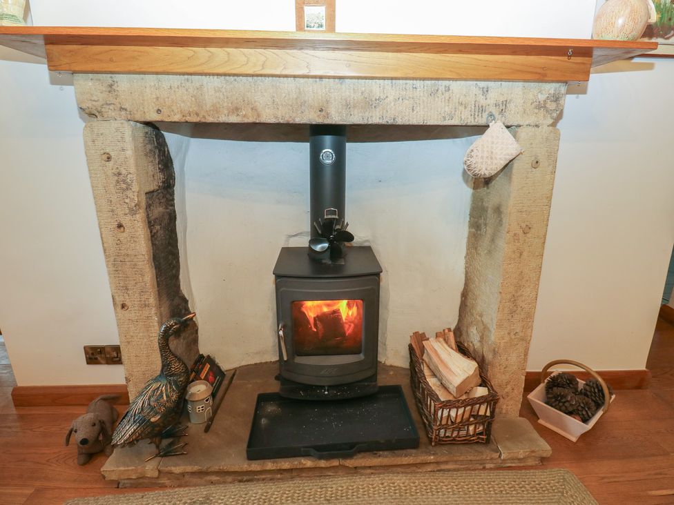 A fireplace with a wood stove and storage basket at Barley Cote Farm in Riddlesden