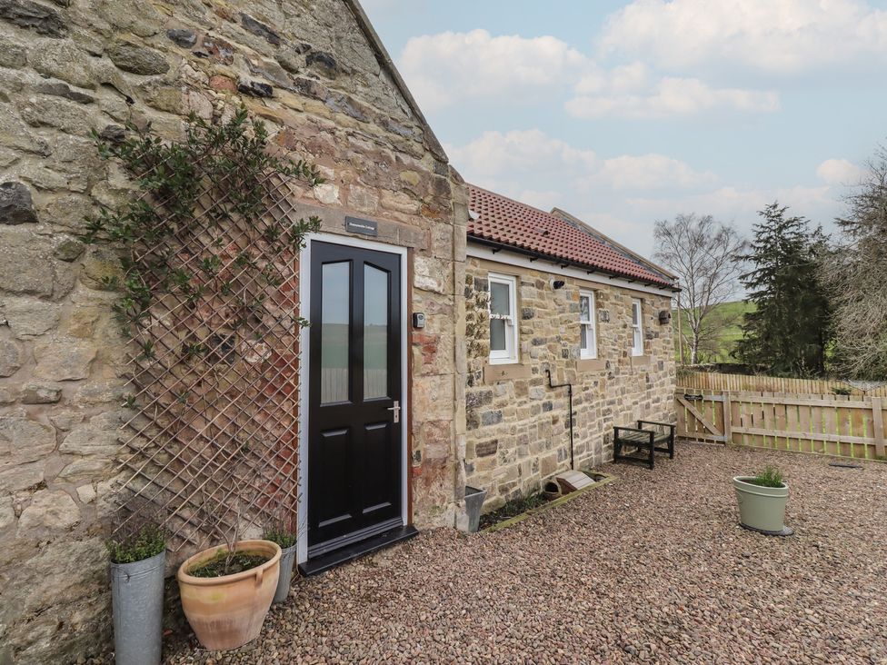 An outdoor entrance with a black door and stone wall at Honeysuckle Cottage in Crookham near Cornhill-On-Tweed