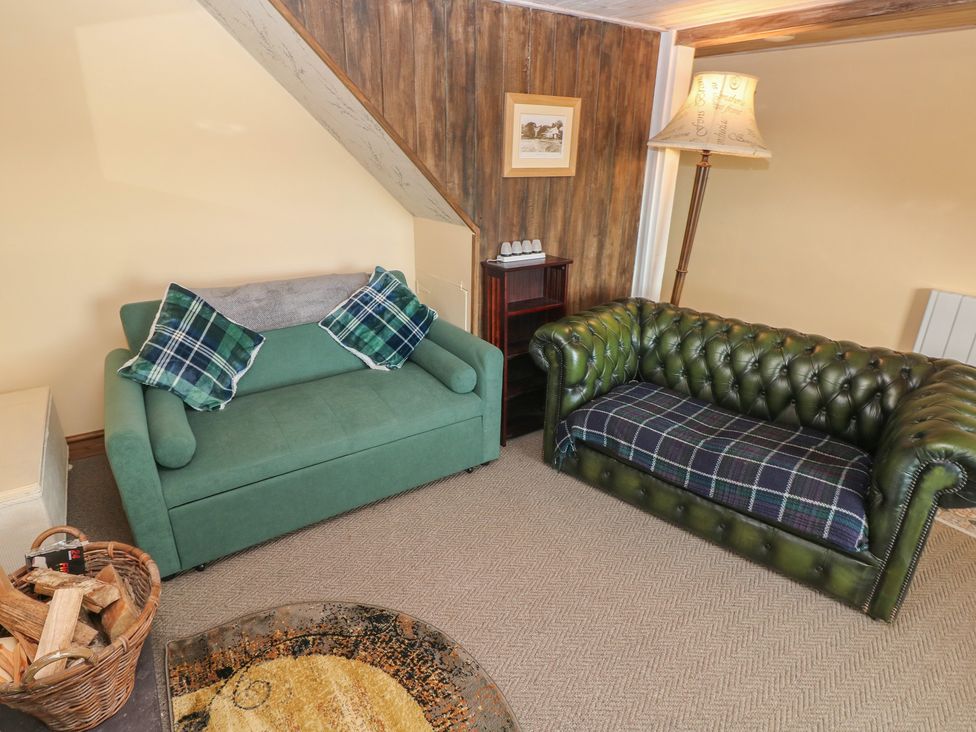 A living room with green sofas and a lamp at 2 Strand Cottages in Carmarthen