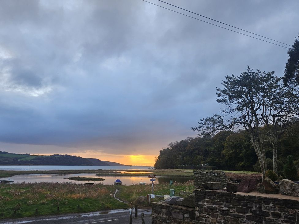 A view of a sunset over water with trees at 2 Strand Cottages in Laugharne