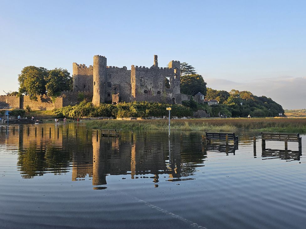 A castle with trees and benches near a body of water at 2 Strand Cottages in Laugharne