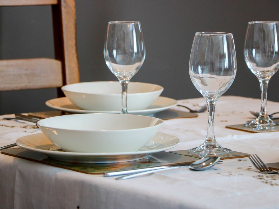 A dining table set with plates, bowls, glasses, and cutlery at Castaway Cottage Maidens