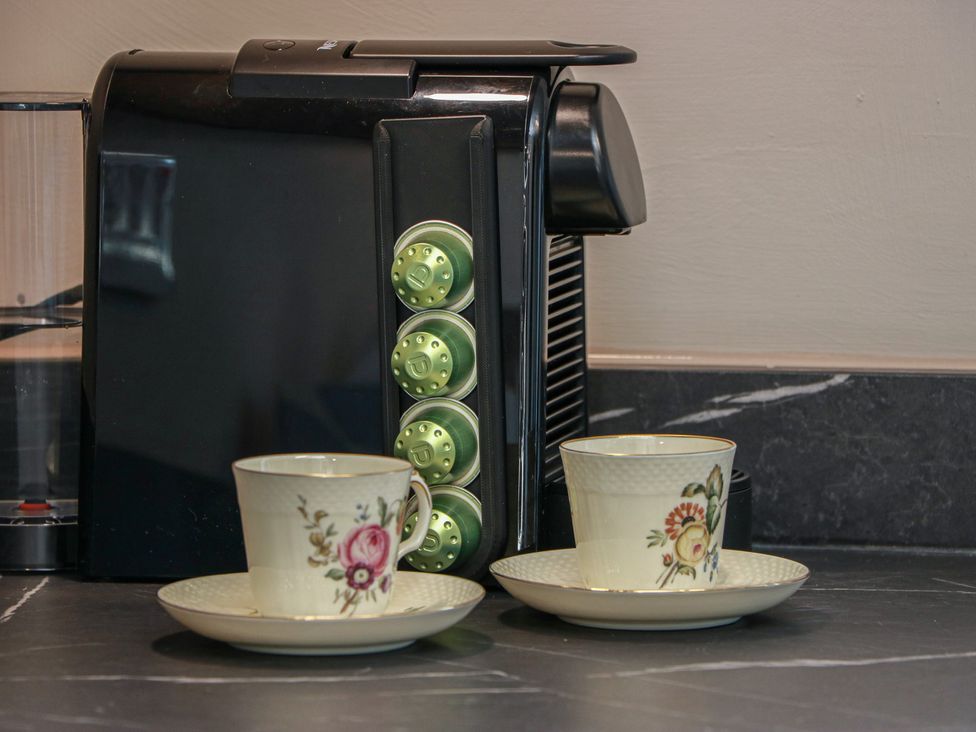 A coffee machine with coffee capsules and teacups on a countertop at Castaway Cottage Maidens