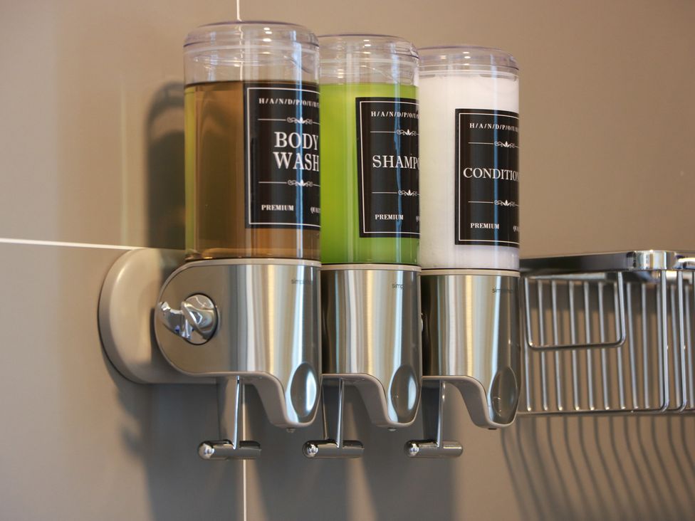 A wall-mounted dispenser with body wash, shampoo, and conditioner in a bathroom at Castaway Cottage Maidens