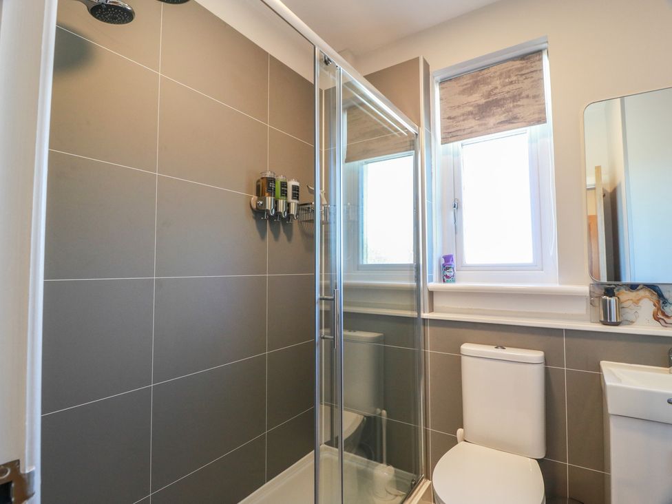 A bathroom with a shower, toilet, sink, and mirror at Castaway Cottage Maidens