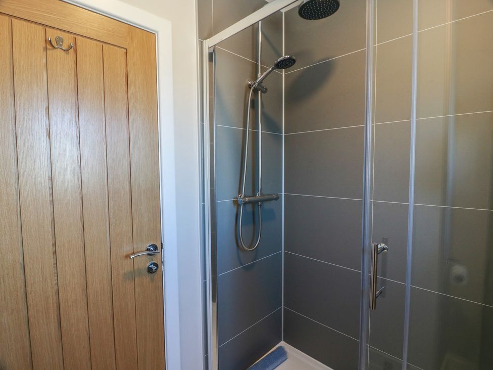 A bathroom with a shower and wooden door at Castaway Cottage Maidens