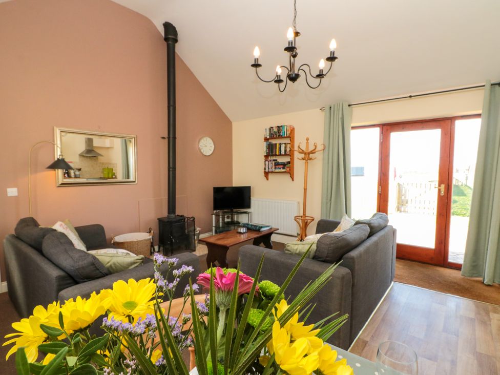 A living room with two gray sofas a wood stove and a TV near double wooden doors at Partridge Cottage neaer Filey