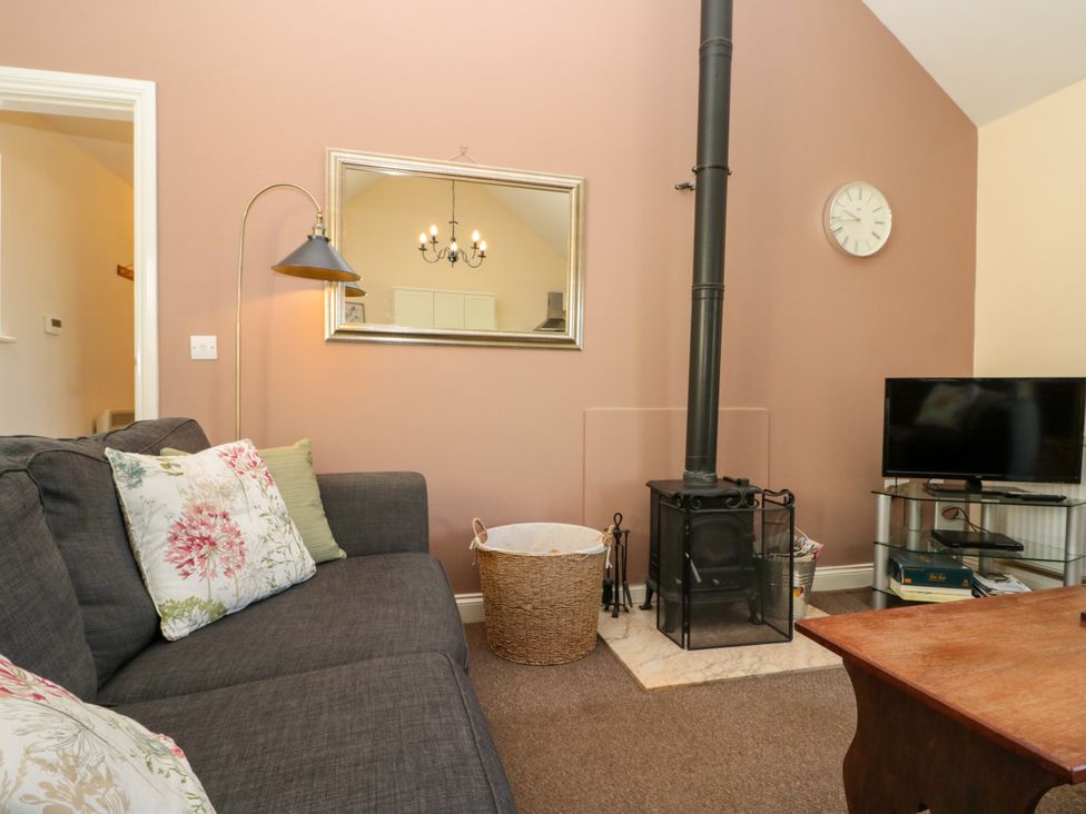 A living room with a gray sofa floral cushions wood burning stove and television at Partridge Cottage neaer Filey