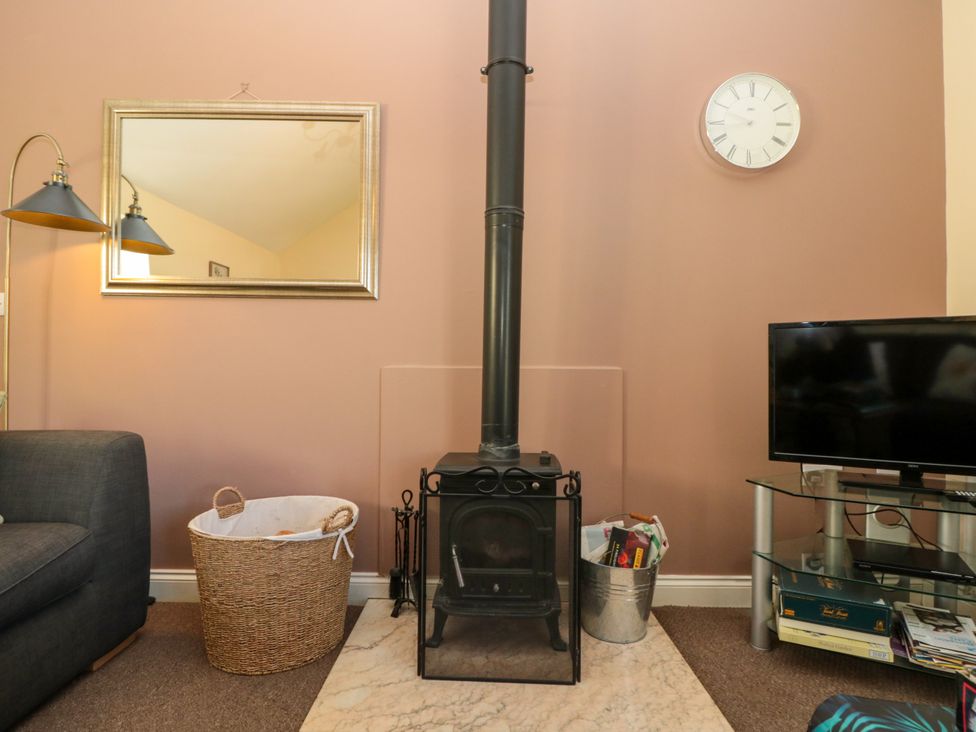 A living room with a black wood stove on a marble hearth a basket to the left a metal bucket to the right a wall clock and a flat screen tv on a glass stand neaer Filey