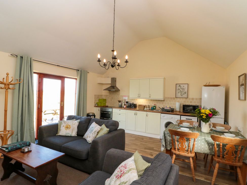An open living room and kitchen with gray sofas a wooden coffee table a dining table with chairs and kitchen cabinets at Partridge Cottage neae Filey