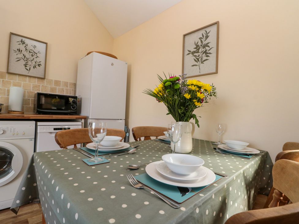 A dining table set with plates bowls and glasses with flowers in a jug in a kitchen with appliances and framed botanical prints at Partridge Cottage neaer Filey