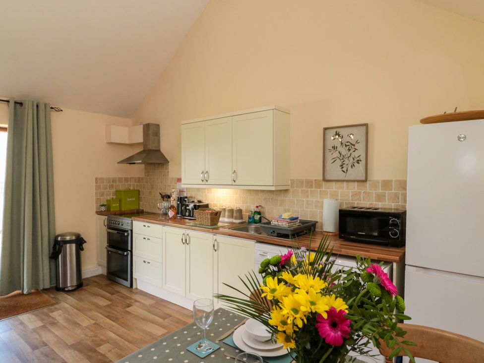 A kitchen with white cabinets and wooden countertops a dining table with flowers and plates neaer Filey