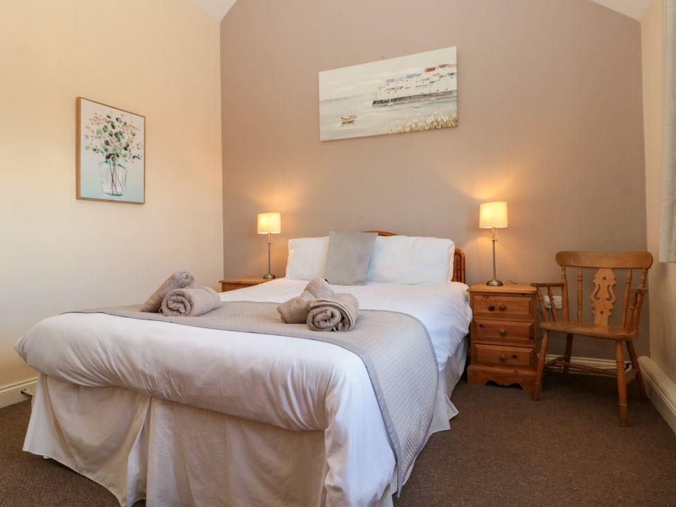 A bedroom with a double bed with towels on it two bedside tables with lamps a wooden chair and artwork on the walls at Partridge Cottage neaer Filey