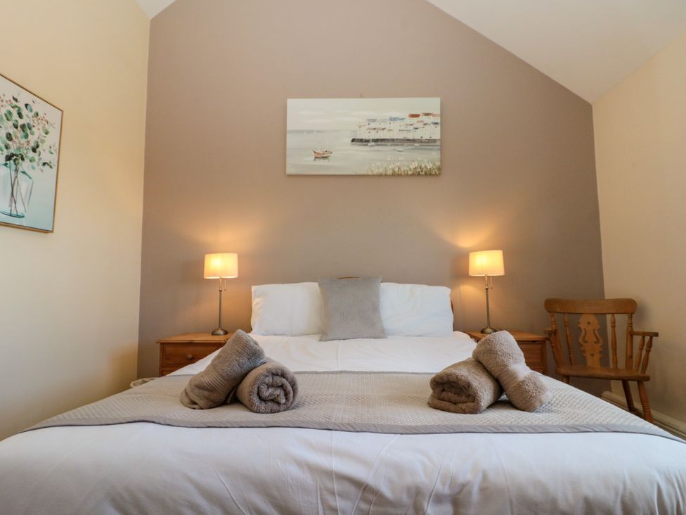 A bedroom with a bed with rolled towels on top two bedside tables with lamps a wooden chair and paintings on the wall at Partridge Cottage neaer Filey