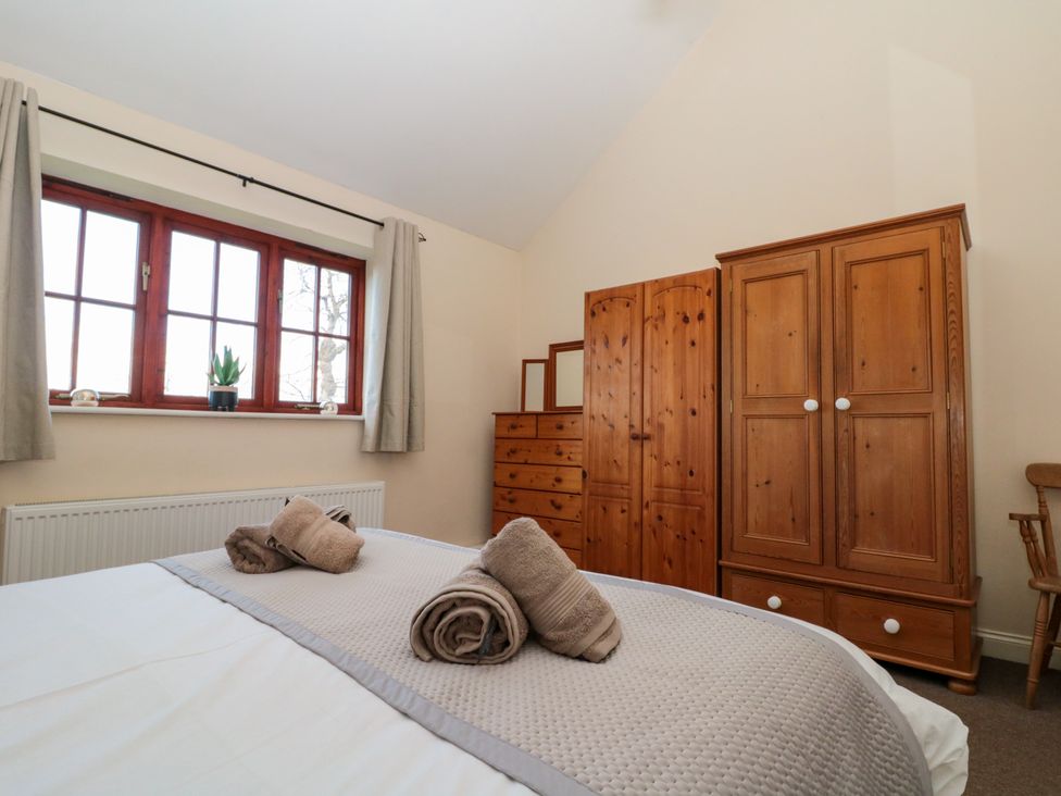 A bedroom with a bed with rolled towels a wooden wardrobe wooden chest of drawers and a window with curtains at Partridge Cottage neaer Filey