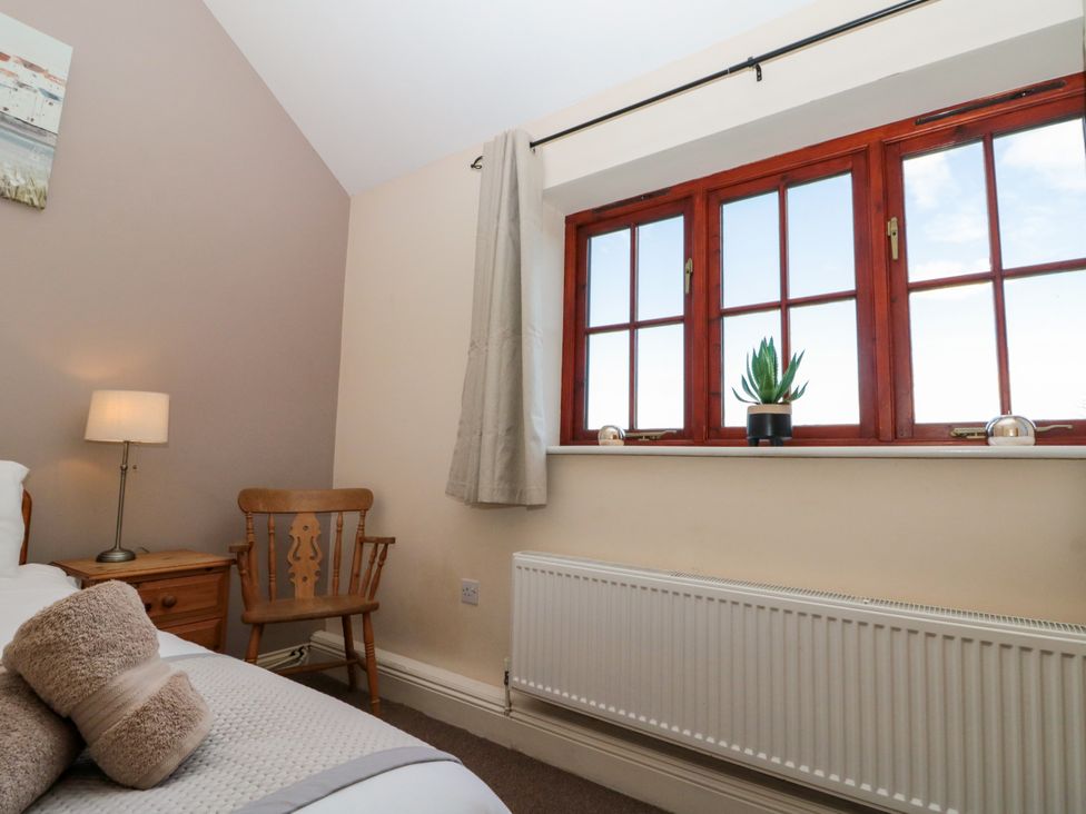 A bedroom with a wooden chair a bedside table with lamp and a window with a plant on the sill at Partridge Cottage neaer Filey