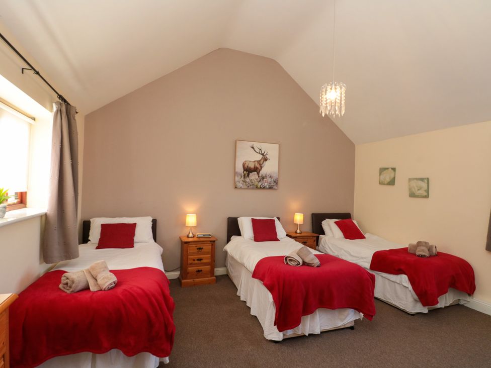 A bedroom with three single beds with red blankets and pillows and two wooden bedside tables with lamps at Partridge Cottage neaer Filey