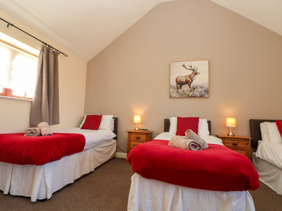 A bedroom with three single beds red blankets and wooden nightstands with lamps at Partridge Cottage neaer Filey