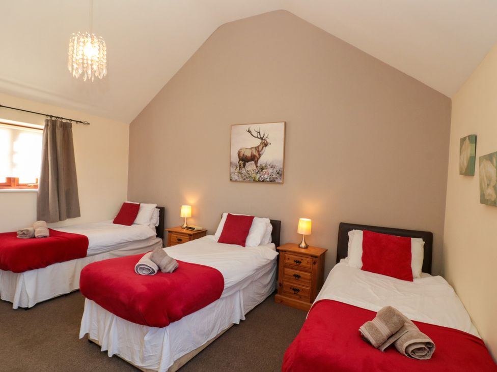 A bedroom with three single beds with red blankets and pillows bedside tables with lamps and painting of a deer on the wall at Partridge Cottage neaer Filey